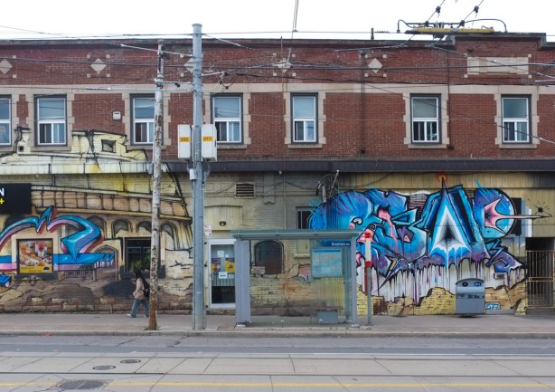 gerrard, at broadview, southwest side, bus shelter, brick building with street art on it