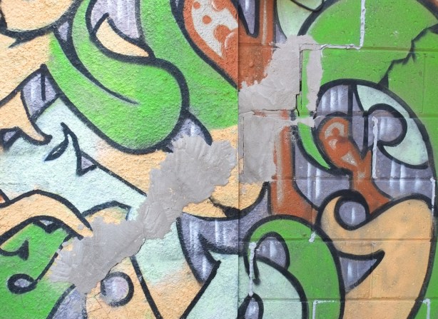 concrete wall with street art, patched over parts of it with grey concrete