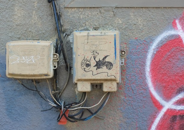 drawing with black marker on electrical boxes on outside of a building