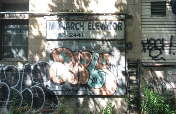 old sign for monarch elevators, in an alley, with lots of shadows, graffiti on wall too