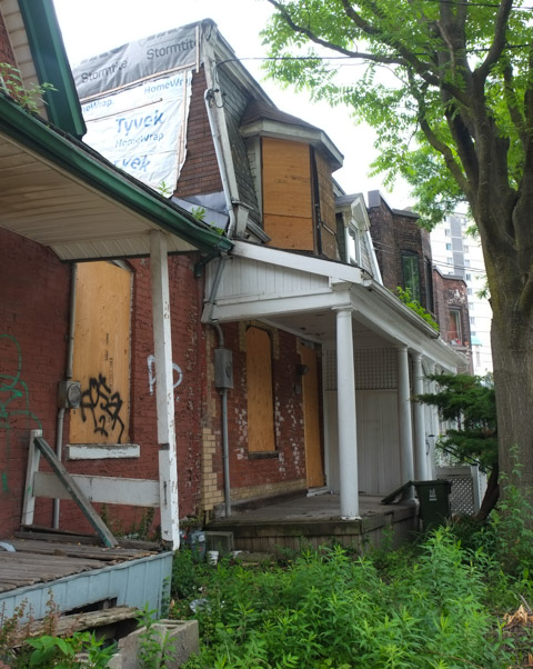 old brick two storey houses with front porches on river street, empty, boarded up with plywood waiting for demolition