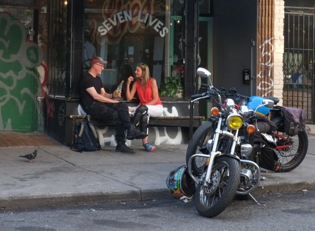 two motorcycles parked, a pigeon on the sidewalk, and a couple at a table outside seven lives restaurant in kensington