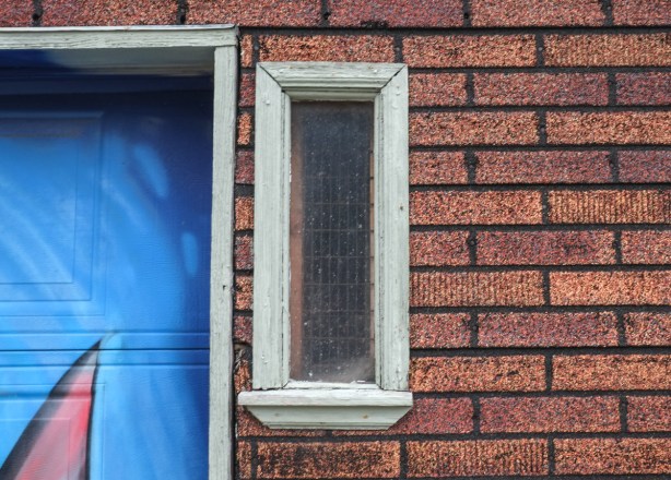 a very small window in a garage clad in fake brick shingles, 