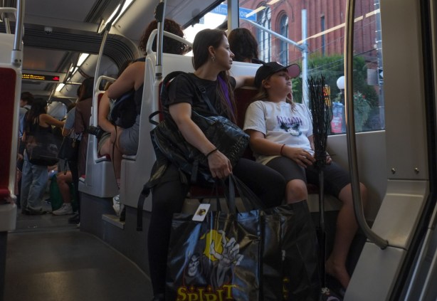 mother and daughter sitting on streetcar, mother with shopping bag from halloween store and daughter holding a black witch's broom