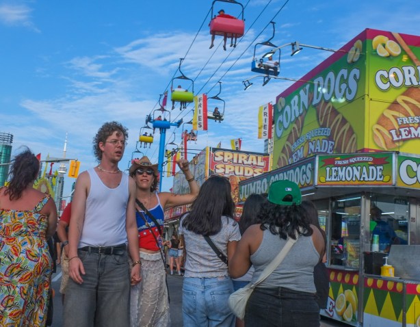young couple walking down the midway, she has a cowboy hat on and a sleeveless shirt with american stars and stripes, Canadian National Exhibition