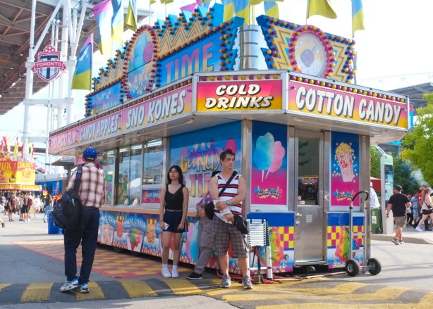 food stand at the ex, cotton candy, cold drinks, sno cones two people standing outside of it, looking grumpy
