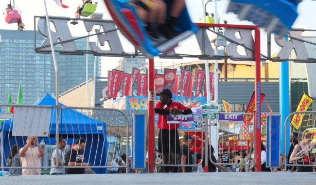 young man, ride operator, standing at side by exit gate watching the crowds