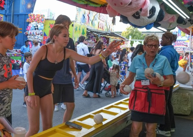 a young woman in black shorts throws a baseball in attempt to get it to land in basket to win game on the midway