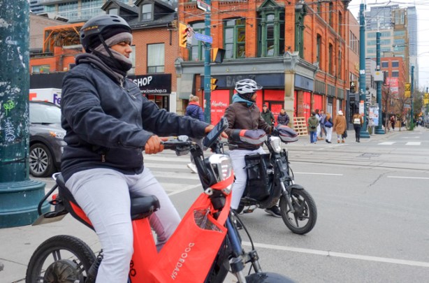 two young men on bikes wait at a red light, on Queen West at Spadina