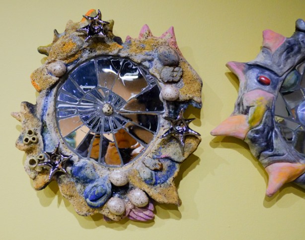 small ceramic artwork hanging on a wall, center is spiral of broken glass, outer layer is shells and rocks but made of ceramics
