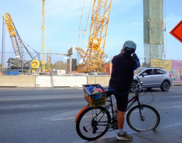 a man on a bicycle has stopped to take a picture of the construction at pape station, on the danforth