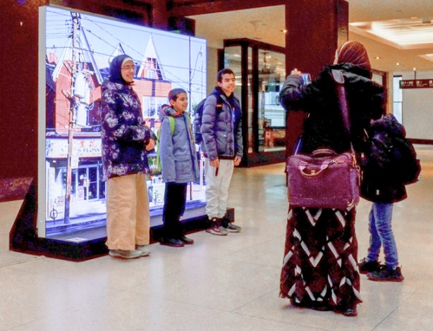 a family stops in front of an art piece at union station, mother is taking a picture of three kids standing in front of it