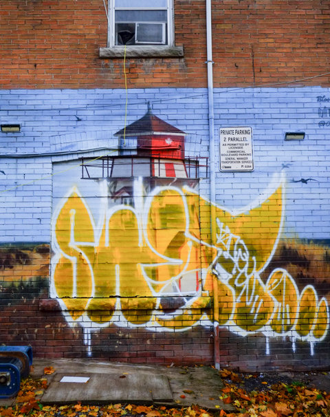 mural of lighthouse on a red brick wall, bottom part has been tagged over with a lot of yellow paint