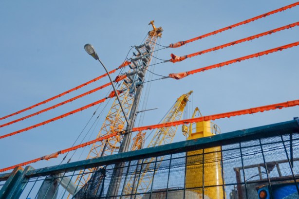 wires covered with orange plastic, on a pole above a construction site