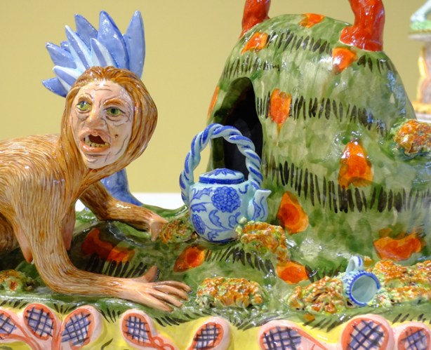 part of a sculpture by Lindsay Montgomery, a male character crawling towards a blue and white teapot sitting on the ground, a matching tea cup is lying on its side