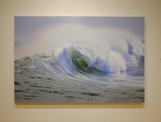 in abbozzo art gallery, on wall, a painting by Katharine Burns of a cresting wave and a small rainbow that is caused by sunlight passing through the spraying water