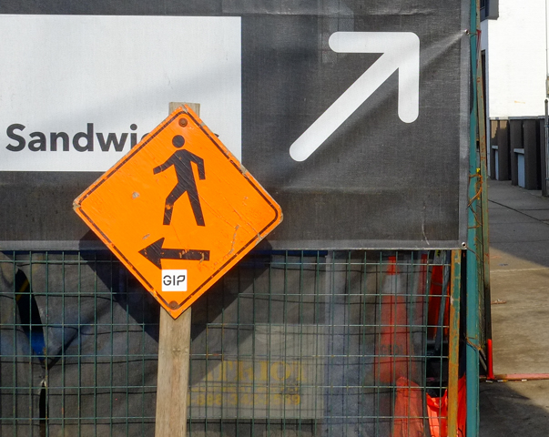 white arrow pointing right and orange pedestrian sign pointing left