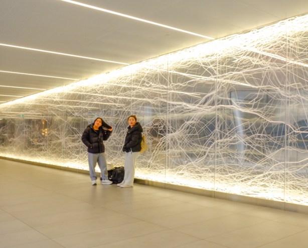two young women stand beside an illuminated artwork, mycelium, by Nicholas Baier, in pedestrian bridge over Bay street
