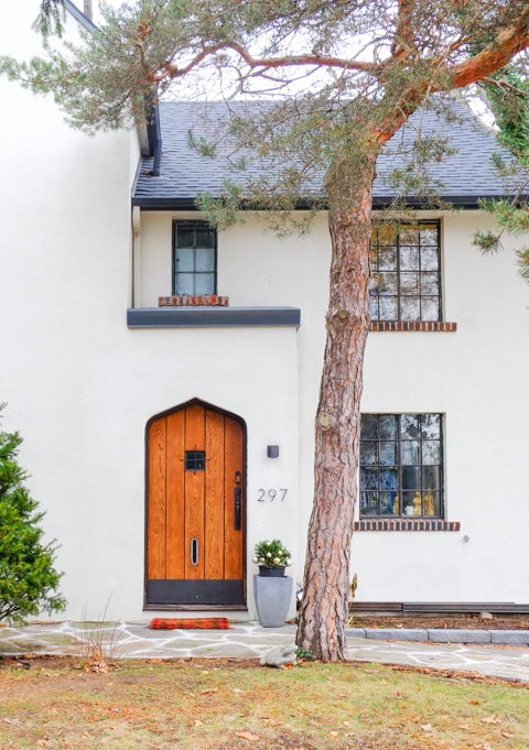 front of a white stucco house with a wood door, tree in front of house