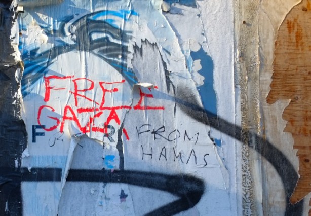 layers of ripped graffiti paste ups and posters on wall of an abandoned building , someone has written free gaza and someone else has added from hamas