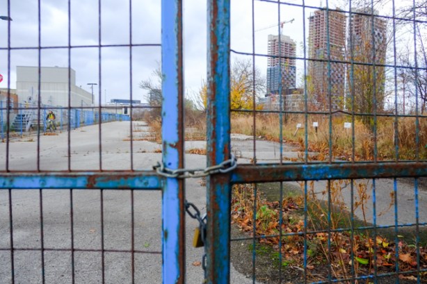 blue metal fence and gate, locked closed, vacant lot beyond the fence