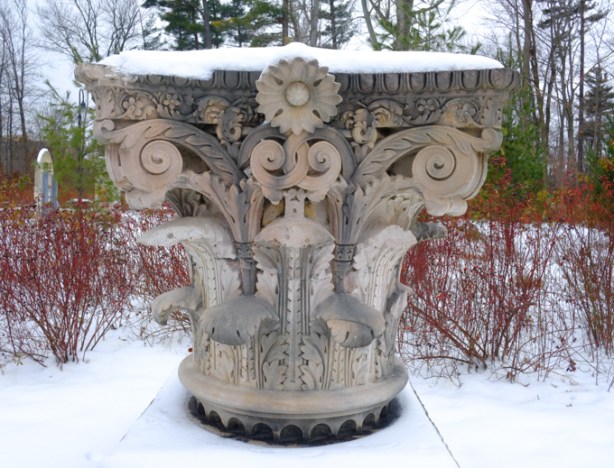 old carved stone top of a column, now resting a park, winter, with red dogwood branches among the dead leaves and leafless trees