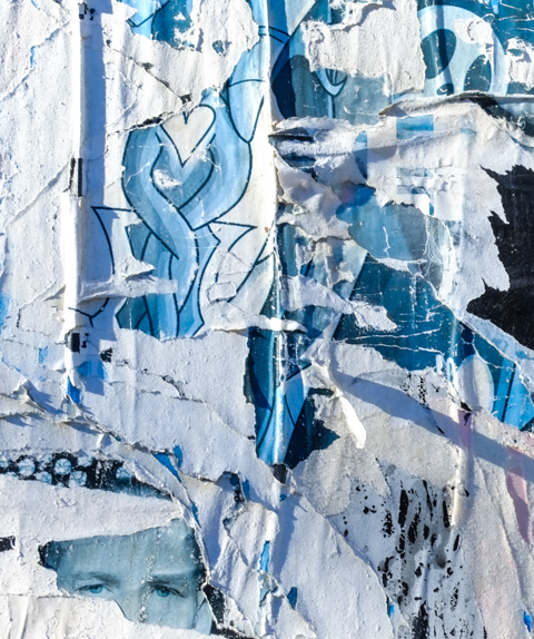 layers of ripped graffiti paste ups and posters on wall of an abandoned building, including a braid and a small heart