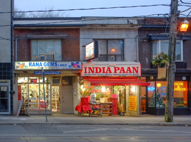 2 store fronts on gerrard, India Paan, and  both are two storey older buildings, 
picture taken late afternoon, lights on inside stores