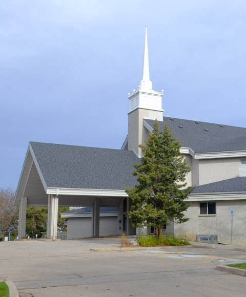 side view of front of Toronto Korean Presbyterian church, large roof over entrance, small white steeple, light grey brick building.