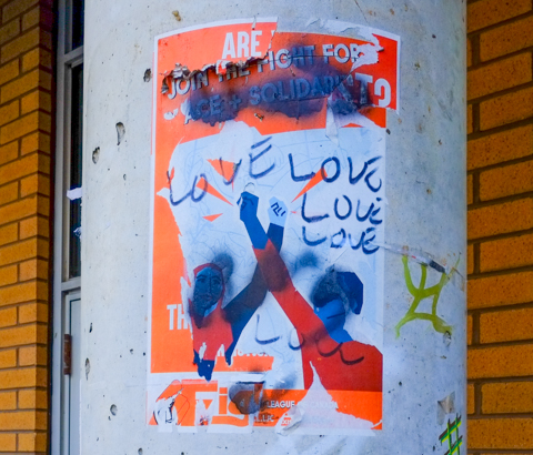 graffiti on a pole with two people with arms upraised, lone has written love, love, love, on it in black marker