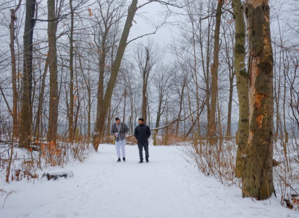 two men talking together while walking on snowy path through woods, in a park