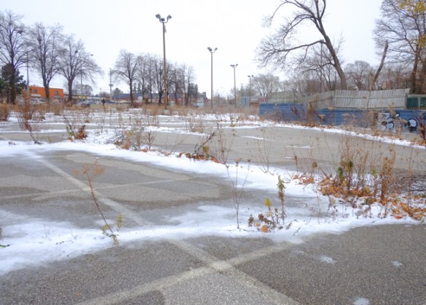 some snow, some weeds growing in the cracks, an old parking lot, with some tall light standards still standing, looking toward Kingston Road