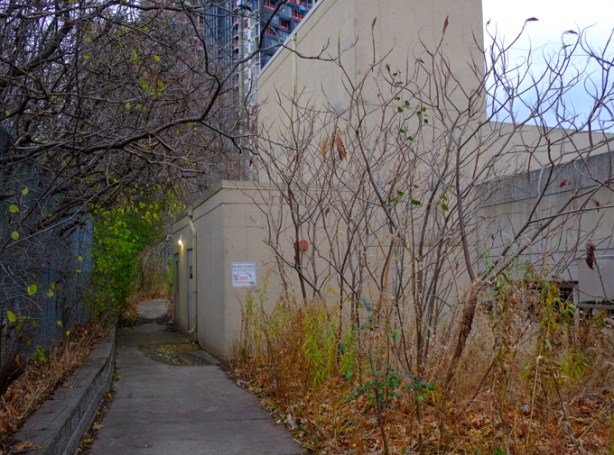 path that runs behind beige concrete building (parking garage) with no trespassing sign)