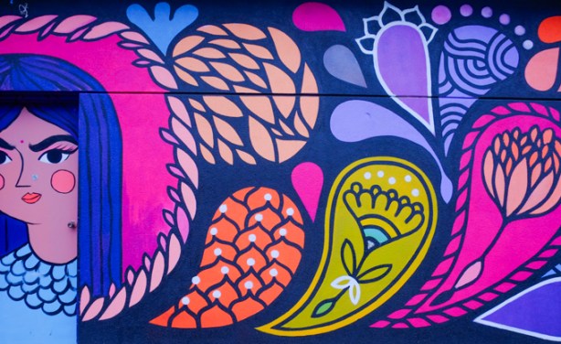 part of a mural, a woman's portrait on a door, with colourful designs around her, leaves and flowers, stylized