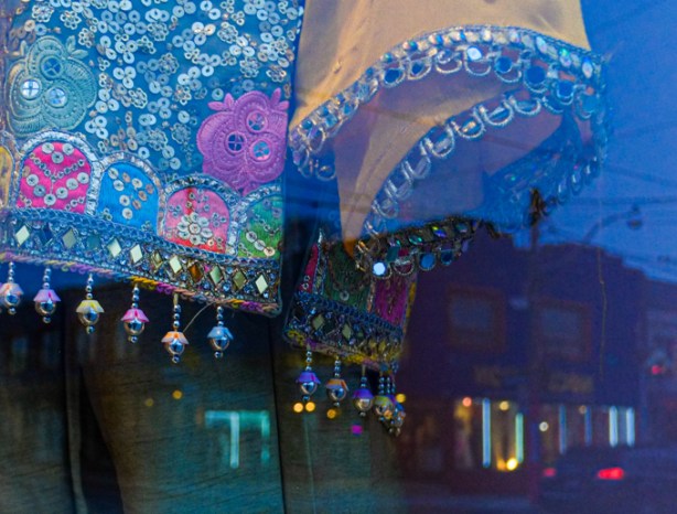 reflections of stores and lights in a window with saris and clothes with shiny beads on fringes, metallic threads, 