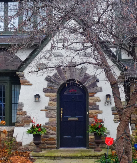 white stucco house with a front door with a curved top, door frame is stone, small christmas decorations beside door