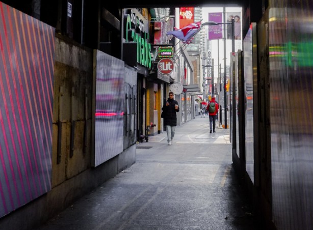 people walking on sidewalk, approaching covered scaffolding at construction site