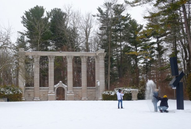 photo session, two people throwing snow while a third takes pictures, backdrop is old stone columns in a park setting