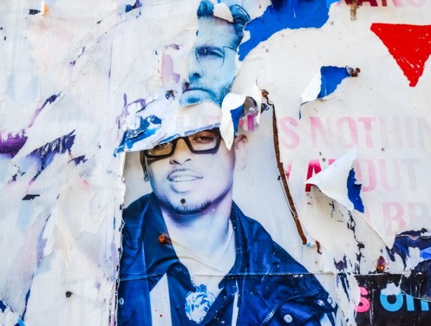 bits and pieces of posters that have been put up on boarded up window on abandoned building, layers, including partial faces of two men