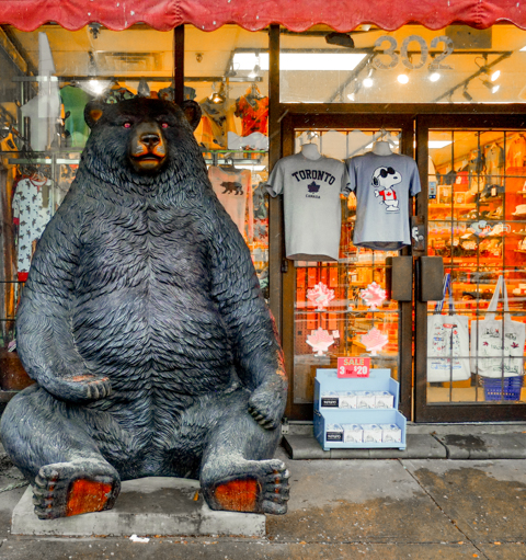large sculpture of a black bear sitting outside a chinese store, evening, lights on inside