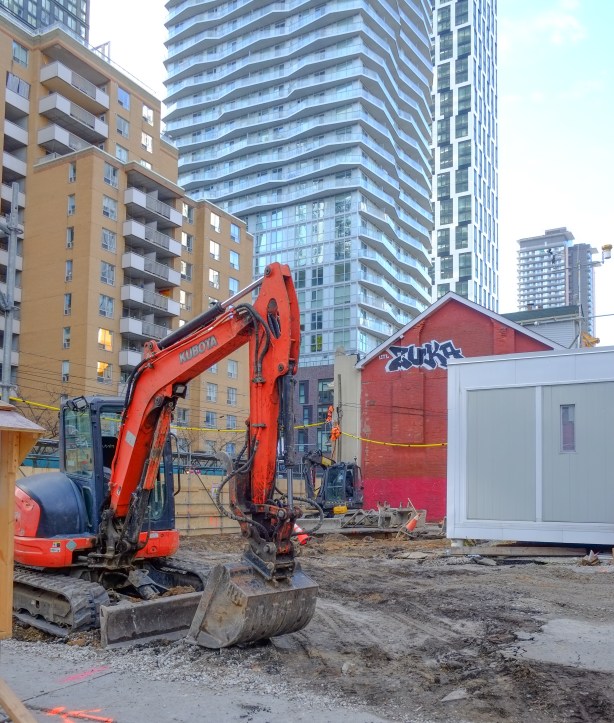 digger in vacant lot at dundas and mutual, old red brick structure with new condos in the background