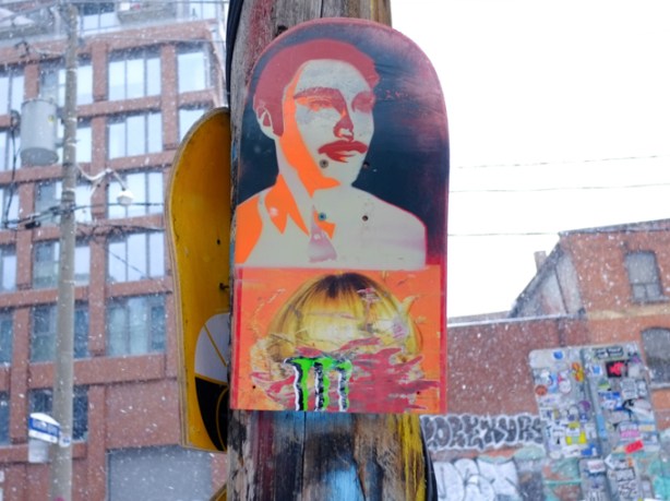 man's portrait painted on half of a skateboard, attached to a pole in graffiti alley
