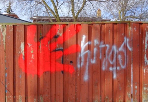 a big red handprint painted on a wood fence, as seen in an alley