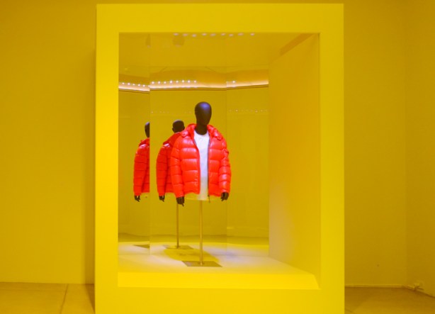a mannequin with a red puffy jacket on a pedestal in a niche in a yellow room, mirrors behind the jacket