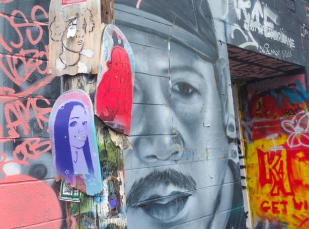 3 skateboard portraits with a large street art painting of a man's face, in grey tones, behind