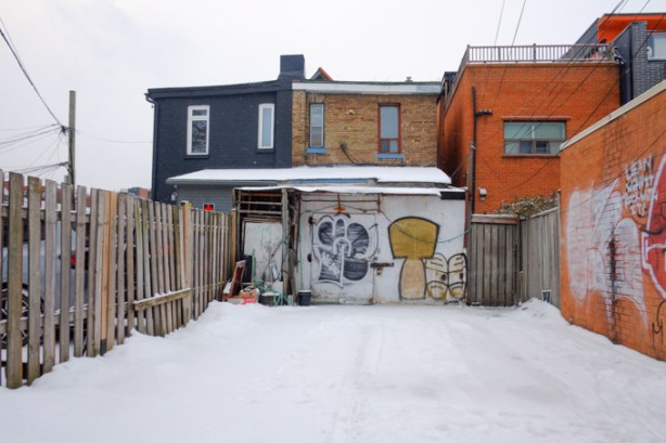 alley scene, back of houses, parking spaces, fence, snow, graffiti