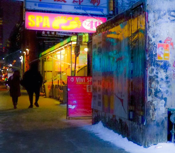 dundas in chinatown, after dark, people on sidewalk, reflections on the wall, pink sign over door that says spa