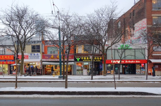 looking across spadina avenue, trees in median, winter, line of stores on the other side, lights on, late afternoon