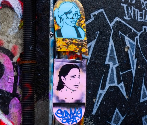 two women's portraits on a skateboard. Top one is turquoise and the bottom one is pink