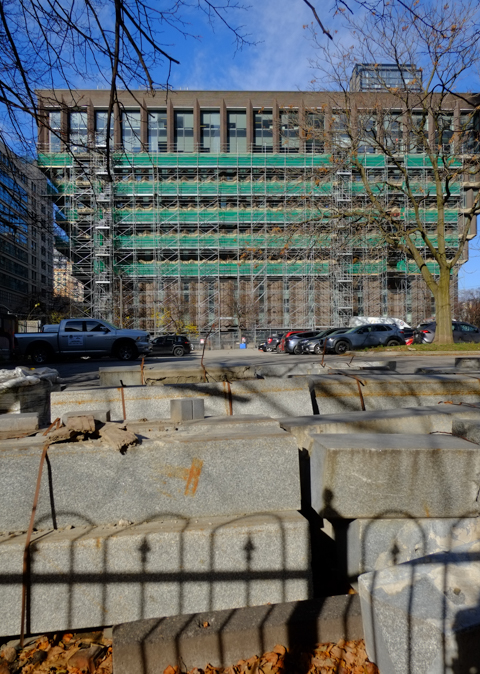 wrought iron fence in front of a large parking lot which is front of a modernist concrete building in upside down triangle shape